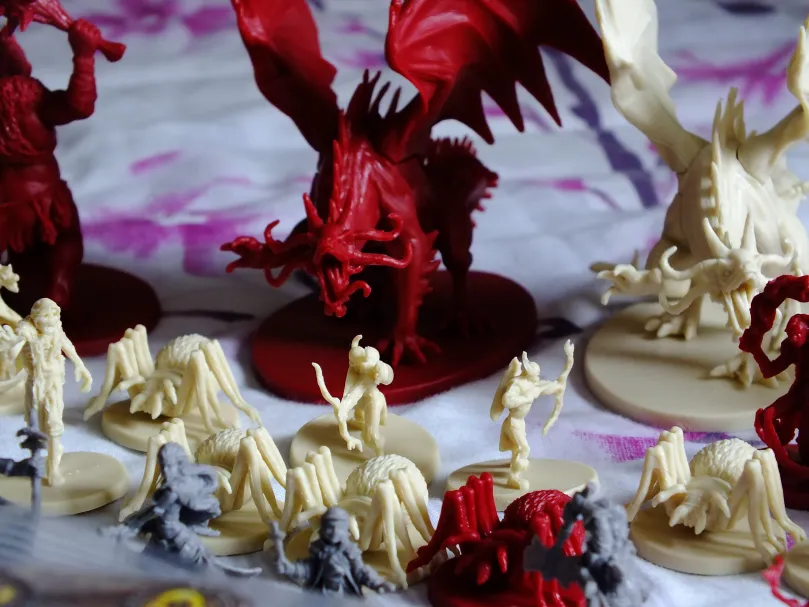 Hero and monster miniatures: small gray heroes, cream creatures, and large red demons including a dragon